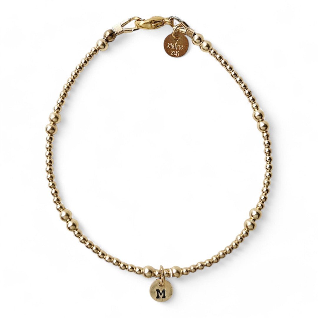 Gouden dames armband Pip met 3en 2mm gouden kraaltjes afgewisseld, in het midden van het armbandje hangt een gouden initiaalbedeltje van 6mm